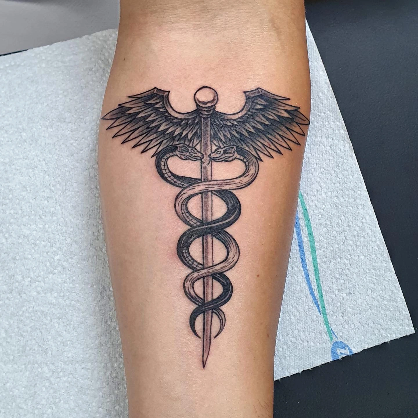 Tatuaj cu simbolul caduceului pe antebraț, cu două șerpi și aripi