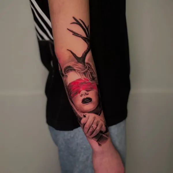 Tatuaj pe braț cu portret de femeie având o bandă roșie peste ochi și coarne de cerb.