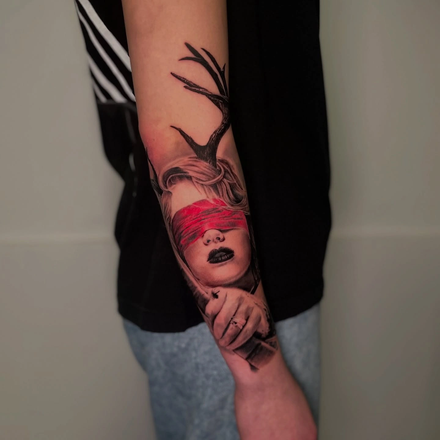 Tatuaj pe braț cu portret de femeie având o bandă roșie peste ochi și coarne de cerb.