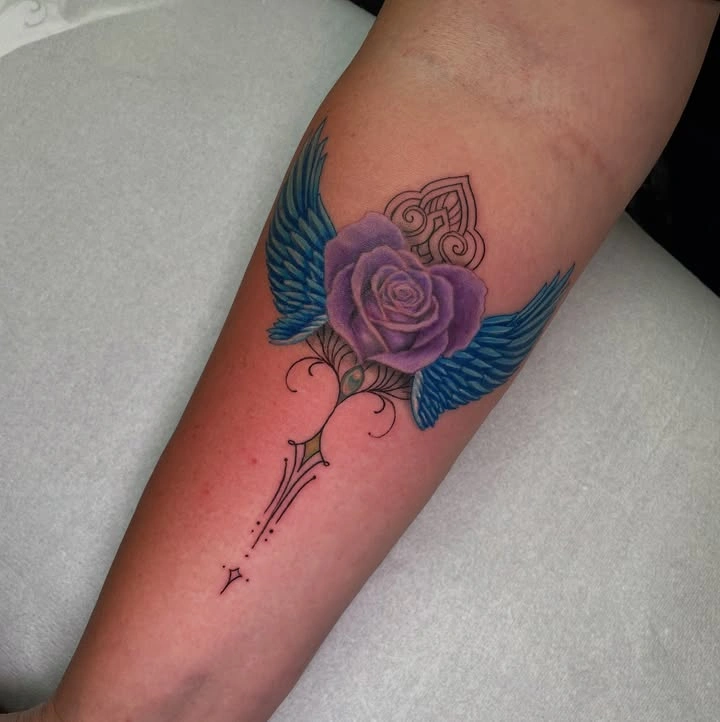 Tatuaj pe antebraț cu trandafir violet și aripi albastre