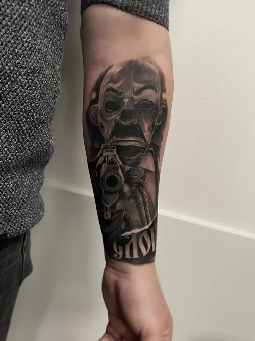 Tatuaj pe antebraț cu o mască și un pistol în stil realist