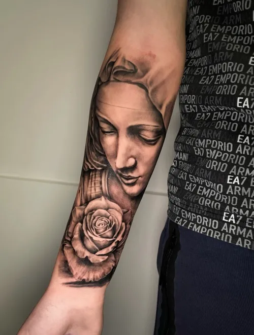 Tatuaj pe antebraț cu portret religios și trandafir.