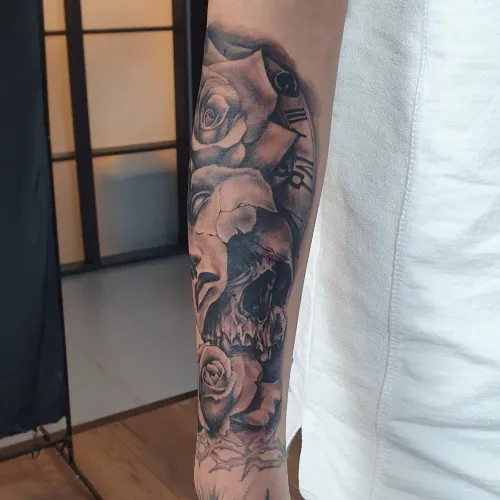 Tatuaj pe antebraț în stil black and grey, cu craniu realist, trandafiri, elemente de ceas și umbre detaliate.