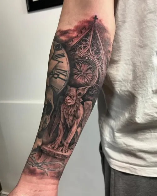 Tatuaj mare pe antebraț în stil realist gotic, cu gargui sculptural, fragment de ceas cu cifre romane și detalii arhitecturale de catedrală, realizat în negru-gri cu accente roșiatice.