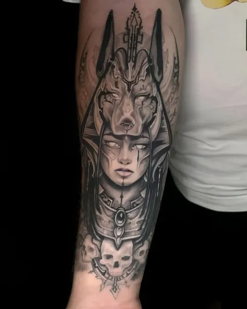 Tatuaj mare alb-negru pe antebraț, cu portret feminin în stil egiptean, mască de Anubis, detalii ornamentale și craniu în partea de jos.