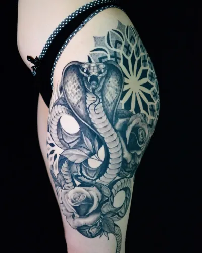 Tatuaj detaliat cu cobră înconjurată de trandafiri și un model mandala, plasat pe coapsă.